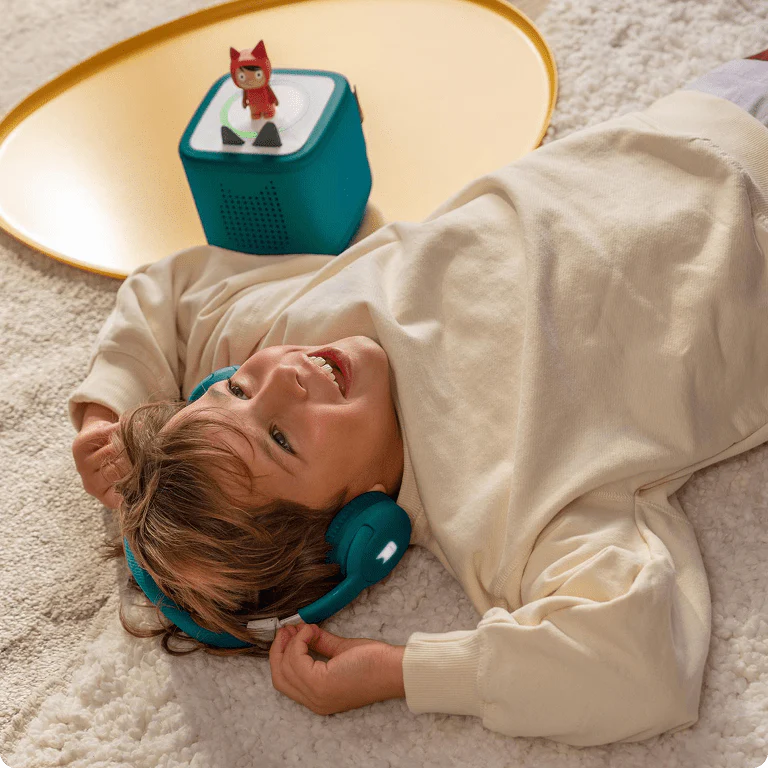 child listening to a Creative-Tonie with a teal Toniebox and teal bluetooth headphones